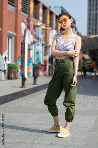 Asian Chinese model girl influencer street shot. Wearing Blue top and army green pants. Street Graffiti background.
