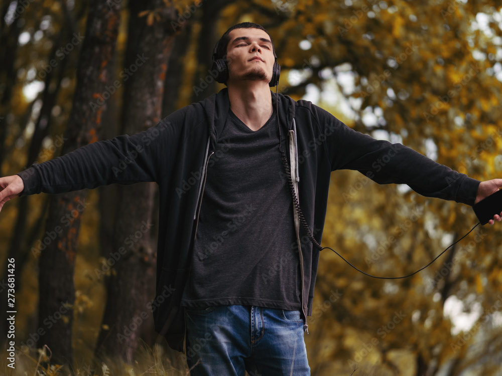 Obraz premium A young man in the autumn forest enjoys listening to music with headphones