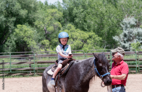 Toddler with a Safety Helmet on Goes on a Pony Ride at a Local Farm with his Horse Being Led by His Grandfather