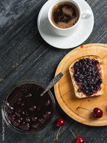 White Cup of coffee and toast with cherry jam on white plate on black table