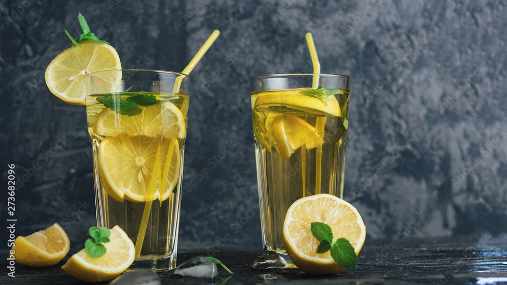 Fototapeta premium Traditional iced, lemon and mint iced tea . Mojito in two glass glasses on a dark concrete table copyspace