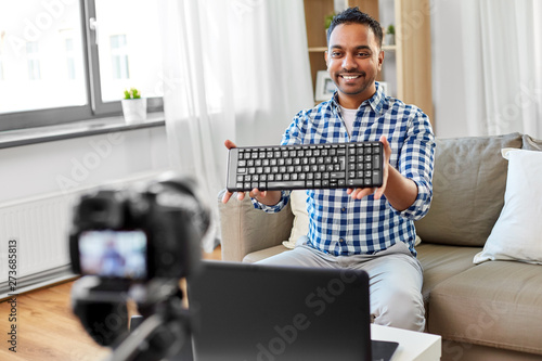blogging, videoblog and people concept - indian male blogger with camera recording video review of computer keyboard at home