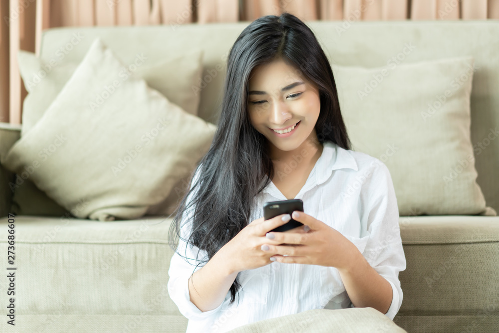 Young Asian woman serving internet she looking a smartphone,messaging and smiling while sitting on carpet near sofa at home,lifestyle,Social networks for sale product, shopping, fashion asia people Young Asian woman serving internet she looking a smartphone,messaging and smiling while sitting on carpet near sofa at home,lifestyle,Social networks for sale product, shopping, fashion asia people