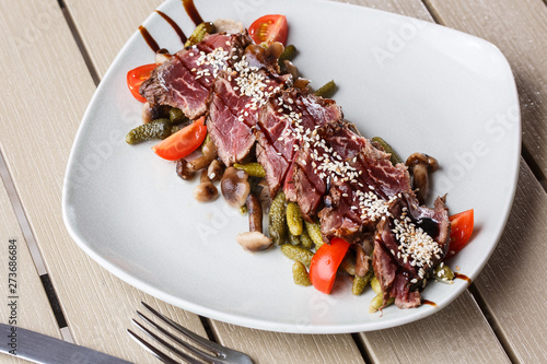 Sliced medium rare Roast beef with pickles, cherry tomatoes,mushrooms on a white plate on wooden background.