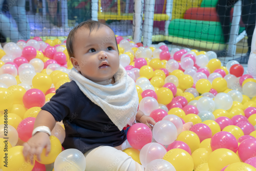 Obraz premium Happy Asian baby girl playing in a big dry pond full with plastic balls, kid at indoor playground