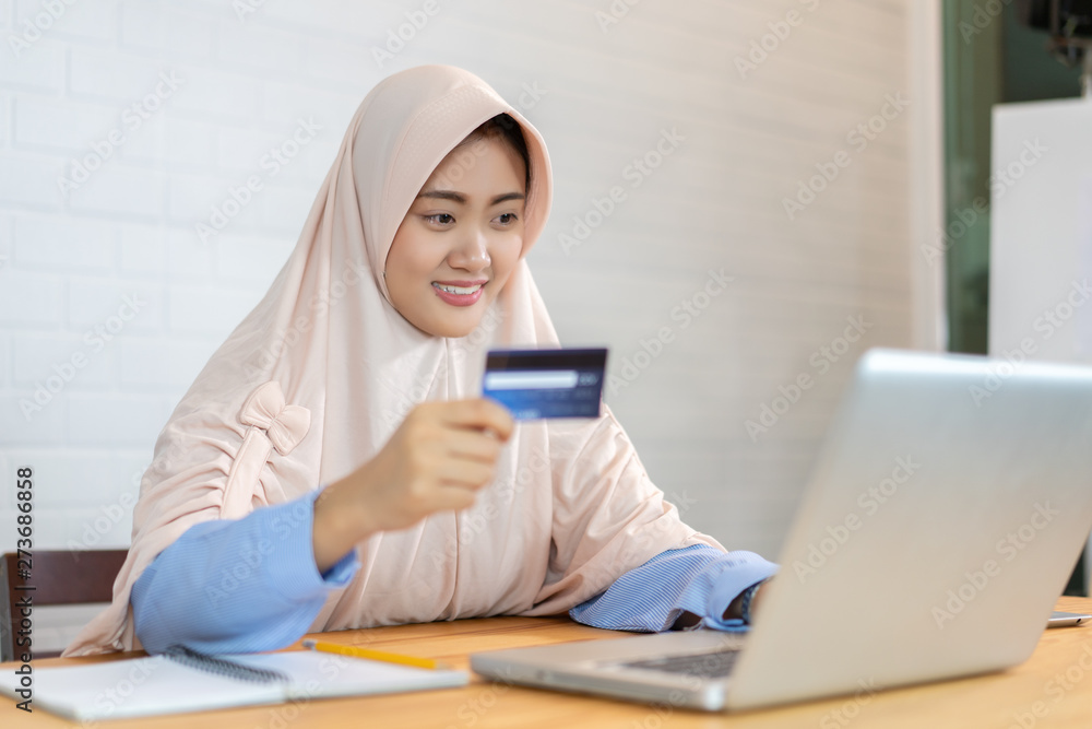 Beautiful Muslim business woman,Arab Female hand holding and show credit card or debit card in office, she uses a laptop computer to shopping online.graphic on credit card for display montage. Beautiful Muslim business woman,Arab Female hand holding and show credit card or debit card in office, she uses a laptop computer to shopping online.graphic on credit card for display montage.