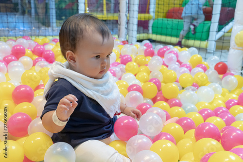 Happy Asian baby girl playing in a big dry pond full with plastic balls, kid at indoor playground