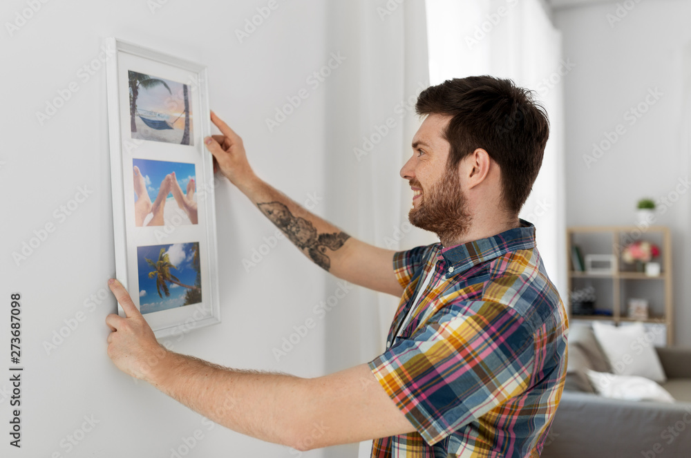 interior decoration and renovation concept - smiling man hanging picture in frame to wall at home
