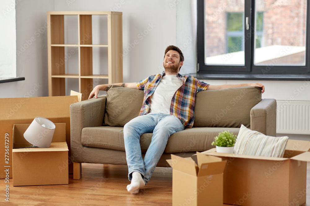 moving, people and real estate concept - happy man with boxes sitting on sofa at new home moving, people and real estate concept - happy man with boxes sitting on sofa at new home