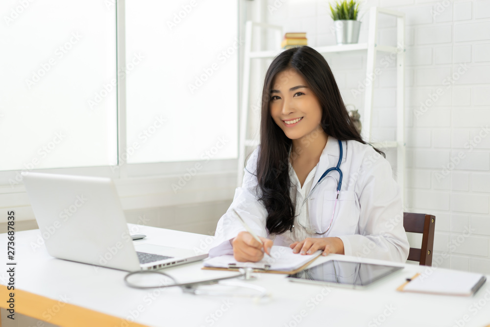 Asian female doctor sitting at hospital office desk giving all patient convenience online service advice and smiling write a prescription to order medical, health care and preventing disease concept. Asian female doctor sitting at hospital office desk giving all patient convenience online service advice and smiling write a prescription to order medical, health care and preventing disease concept.