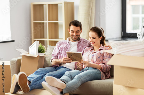 moving, people, repair and real estate concept - happy couple with photo frame and cardboard boxes sitting on sofa at new home