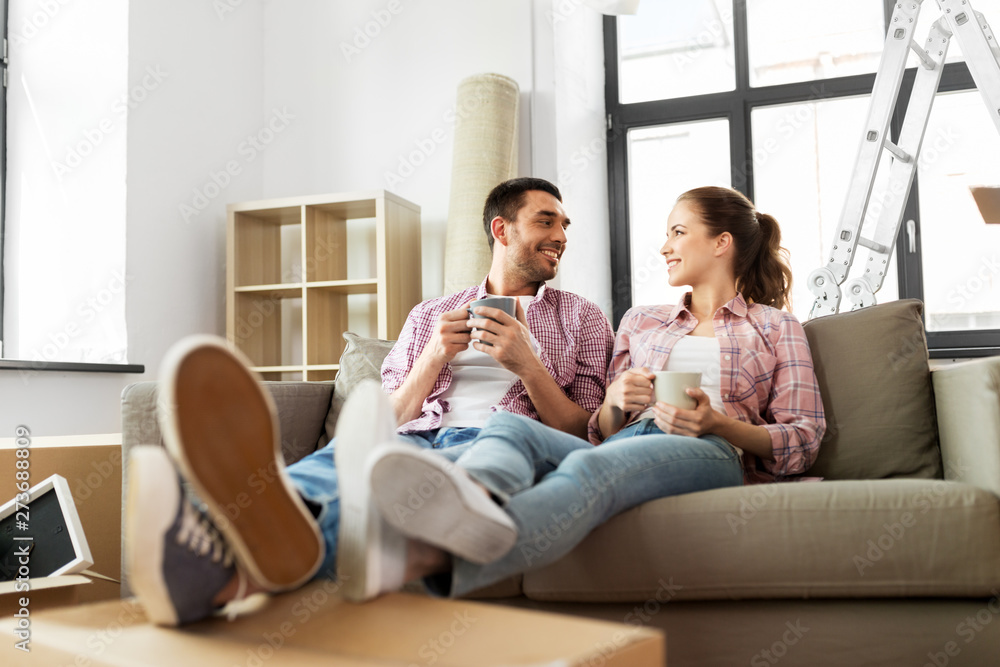 moving, people, repair and real estate concept - happy couple sitting on sofa and drinking coffee at new home moving, people, repair and real estate concept - happy couple sitting on sofa and drinking coffee at new home