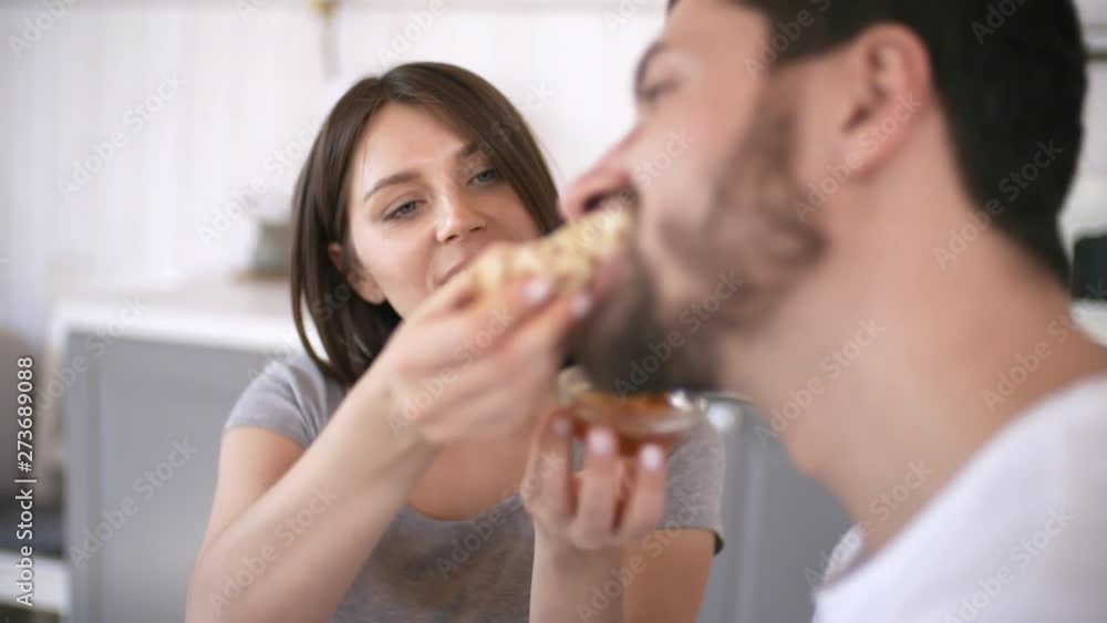Medium shot of young woman feeding pancake with honey to bearded boyfriend, then kissing him on lips Medium shot of young woman feeding pancake with honey to bearded boyfriend, then kissing him on lips