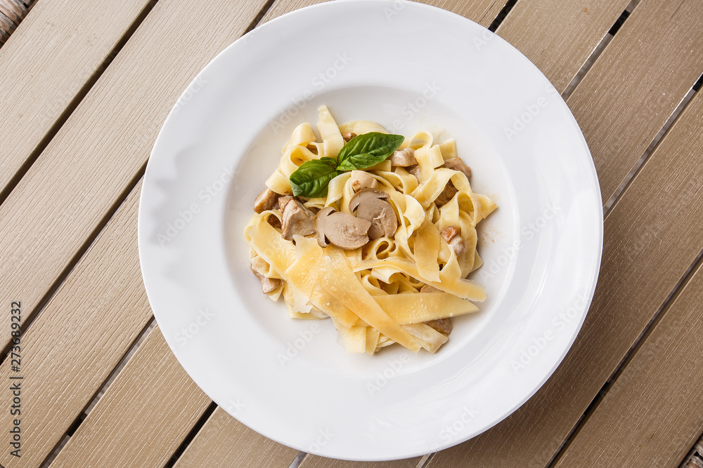 Tagliatelle vegetarian Pasta Dish with Mushrooms decorated with basil. Delicious lunch with pasta and white mushrooms. On wooden background.