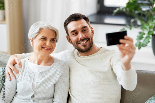 family, generation and people concept - happy smiling senior mother with adult son taking selfie by smartphone at home