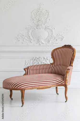 Vintage sofa with wood carvings in a luxurious light interior with stucco on the walls. Selective focus.