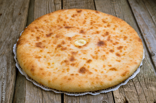 Ossetian pie with cheese on wooden background