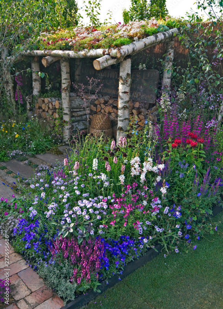 Fototapeta premium A colourful mixed flower border with Monarda 'Cambridge Scarlet' and a Sedum covered roof on a garden shelter