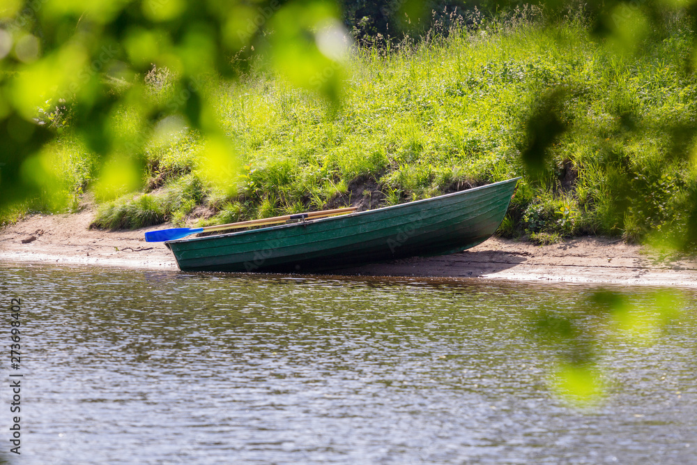 empty green wooden rowboat near the shore on a sunny summer day. rowing pleasure boat with oars near the shore