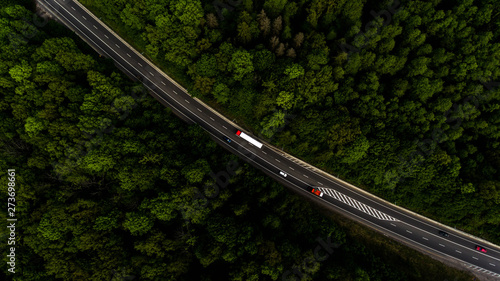 Foto Aerial view flying over road, that lead through the green forest.