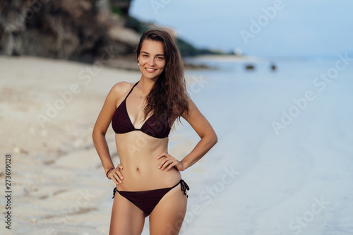 Happy girl with perfect body in black swimwear posing on white sand beach