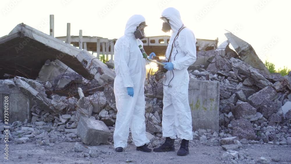 two scientists in protective suits and masks and make measurements of radiation against the background of the ruins at sunset two scientists in protective suits and masks and make measurements of radiation against the background of the ruins at sunset