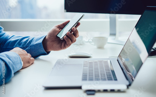 Crop businessman with smartphone at computer desk
