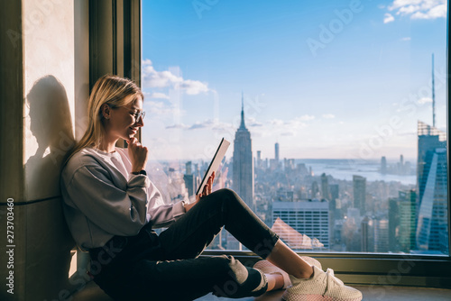 Photography Thoughtful female digital nomad thinking on writing new travel blog article while inspiring by scenery view of New York downtown sitting on window sill in modern  coworking interior