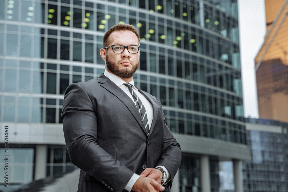 Portrait of a serious business man in a suit and glasses on the background of an office building Portrait of a serious business man in a suit and glasses on the background of an office building