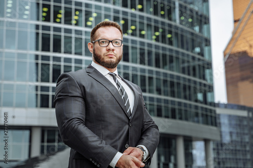 Portrait of a serious business man in a suit and glasses on the background of an office building