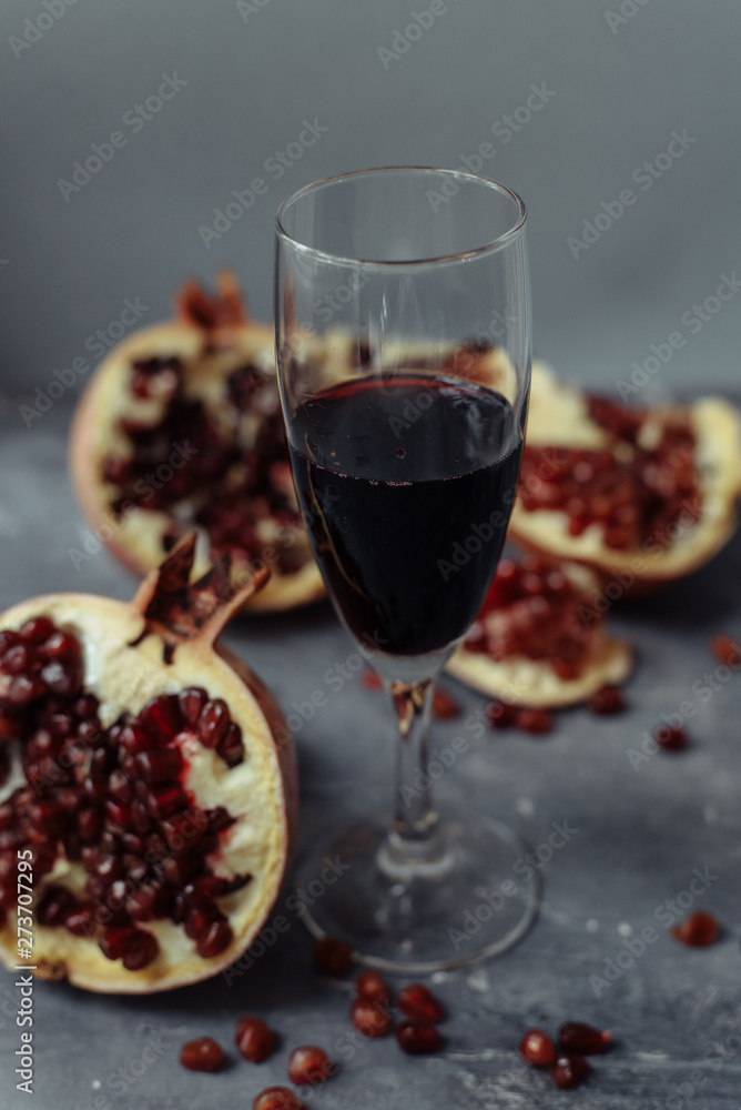 A wine glass with red wine stands on a gray grunge background next to grenades. Fruits and pomegranate wine A wine glass with red wine stands on a gray grunge background next to grenades. Fruits and pomegranate wine