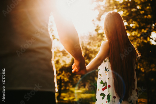 Back view of a unrecognizable woman with long red hair walking outside against sunset in the forest holding hand of her boyfriend.