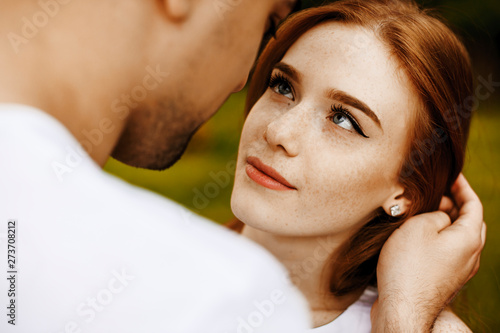 Close up of a beautiful woman with red hair and freckles looking smiling at her boyfriend outside.
