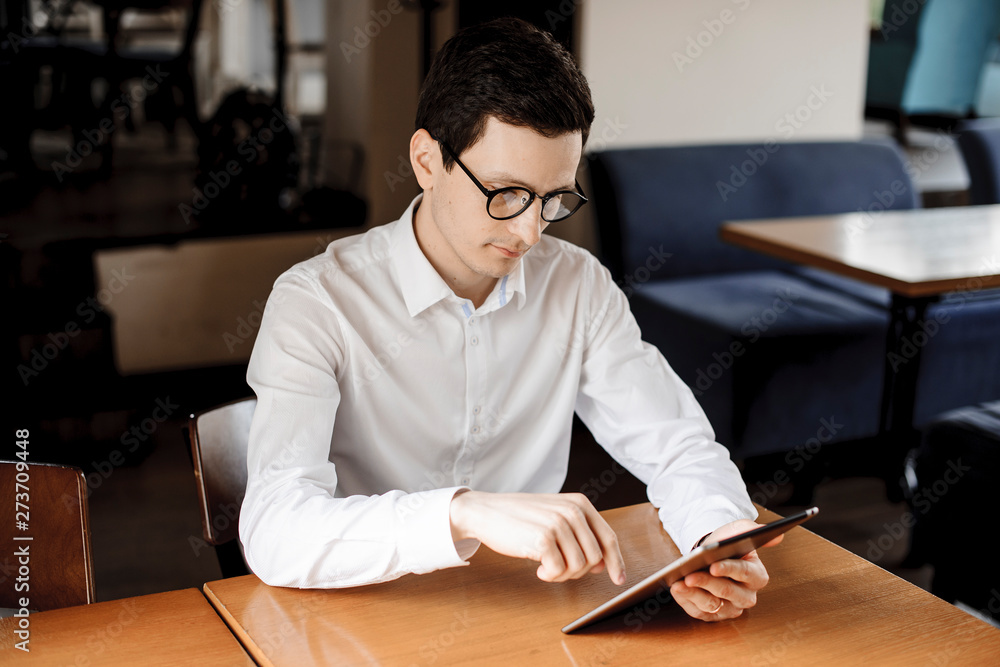 Handsome caucasian businessman operating on a tablet while sitting at a desk wearing eyeglasses and dressed in white shirt. Handsome caucasian businessman operating on a tablet while sitting at a desk wearing eyeglasses and dressed in white shirt.