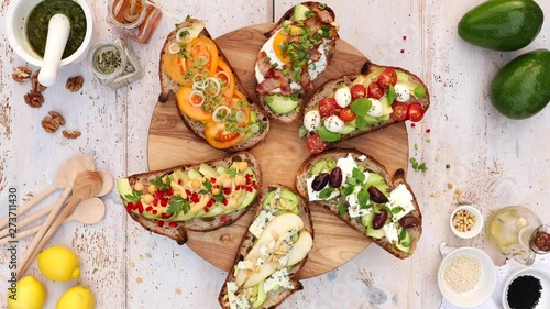 Assorted open faced sandwiches, Open avocado sandwiches made of slices of sourdough bread with various toppings on a round board, on a white wooden table, top view, 4k.