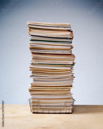 In, out tray on desk with tall stack of never ending office paperwork