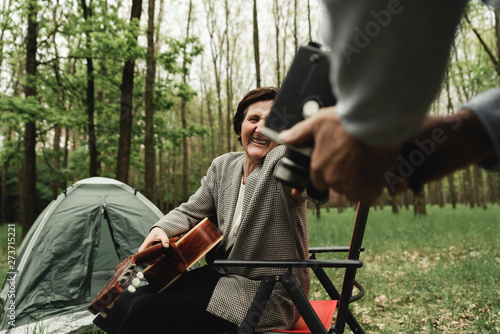 Loving mature couple coming on picnic with guitar. Happy senior couple playing a guitar and having a romantic date on camp. Man with old camera. Happy senior people spending time together on field