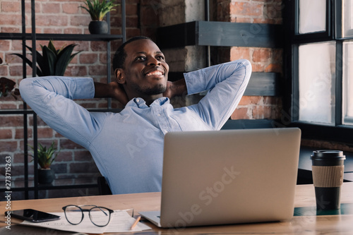 African american business man resting head on hands and spreading elbows, smiling during his break from work