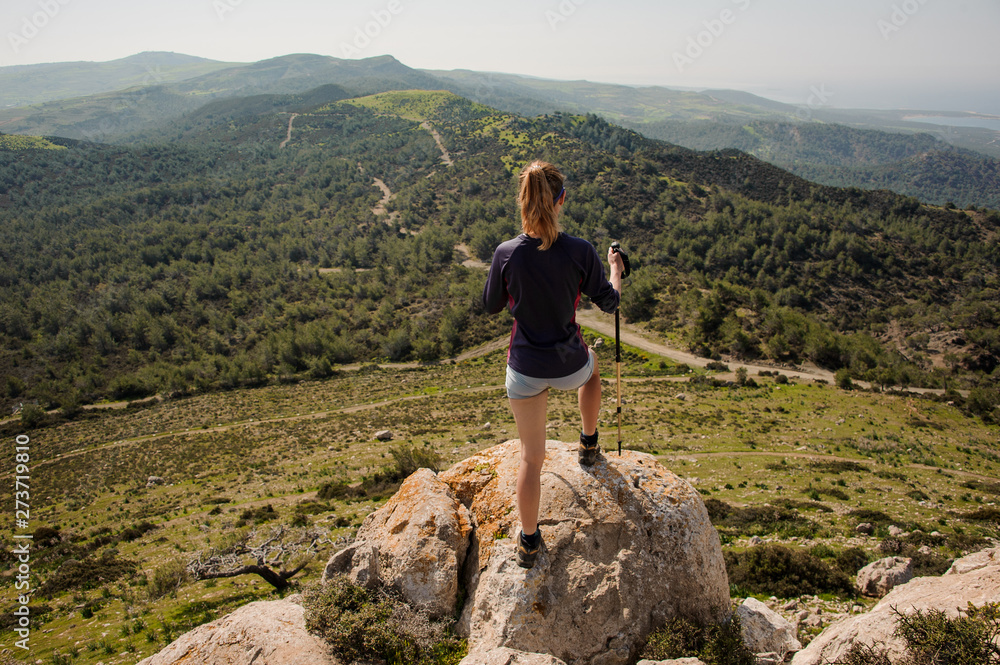 Back view girl standing on the rock in shorts with walking sticks