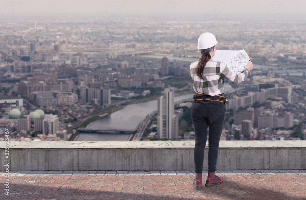 Female engineer holding construction plans standing on the roof top above a city