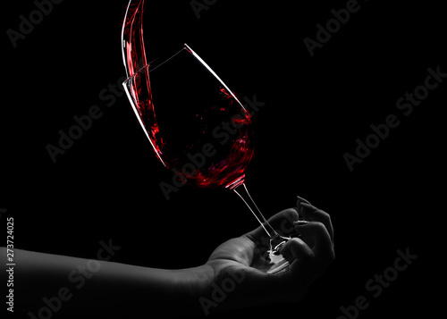 a glass of wine in hand, red wine pours into a glass, an over black background