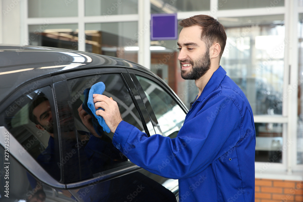 Worker cleaning automobile window with rag at car wash Worker cleaning automobile window with rag at car wash