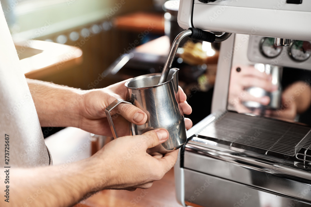 Barista frothing milk in metal pitcher with coffee machine wand at bar counter, closeup Barista frothing milk in metal pitcher with coffee machine wand at bar counter, closeup
