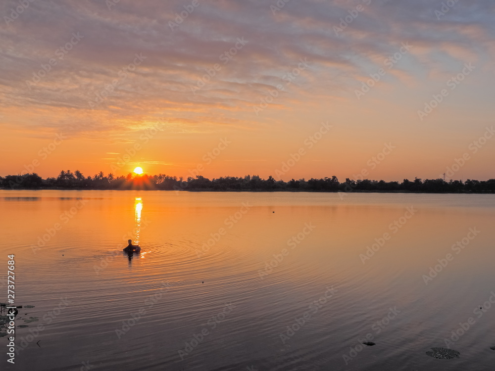 Lake view morning scenic a fisherman floating in water with red sun light and blue sky background, sunrise at Krajub Lake, Ban Pong, Ratchaburi, Thailand.