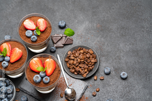 Classic tiramisu dessert with blueberries and strawberries in a glass on stone serving board on dark concrete background