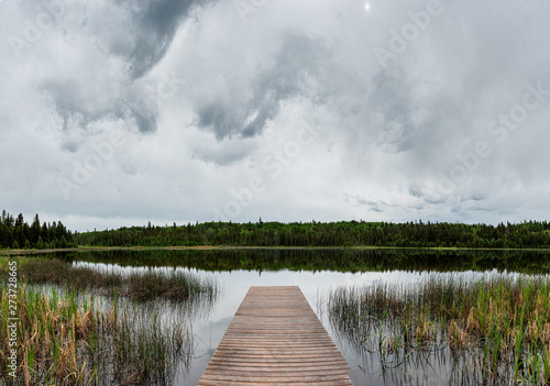 Fototapeta Naklejka Na Ścianę i Meble -  Long wooden dock extending into a calm northern lake with storm clouds in the sky