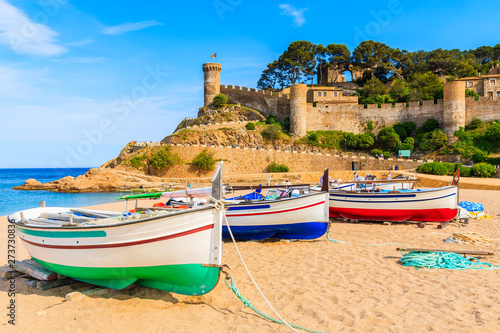 Fishing boats on golden sand beach in bay with castle in background, Tossa de Mar, Costa Brava, Spain