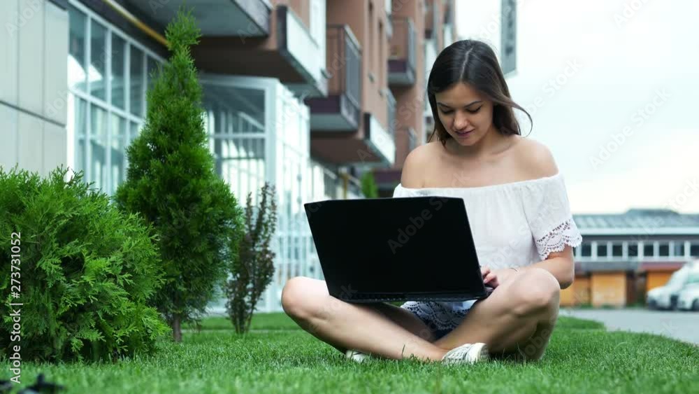 Young beautiful businesswoman typing on a laptop, sitting on the grass near hotel, woman use notebook in the park. Young beautiful businesswoman typing on a laptop, sitting on the grass near hotel, woman use notebook in the park.