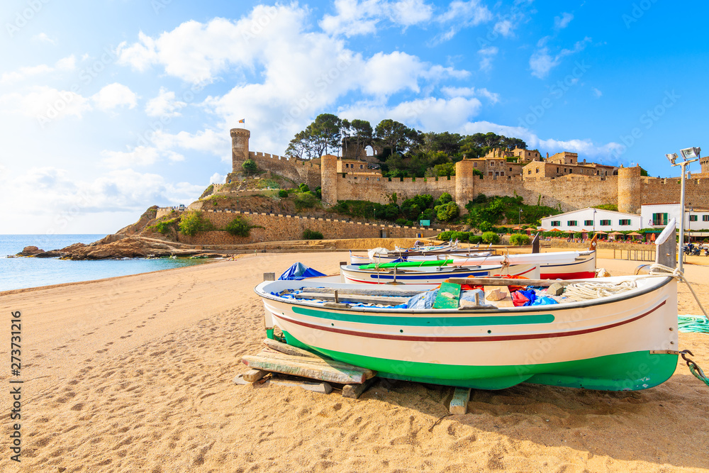 Fishing boats on golden sand beach in bay with castle in background, Tossa de Mar, Costa Brava, Spain