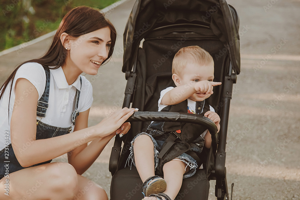 A young single mother, in a park with her son, a boy, in a wheelchair, looks after, cares. A happy family. Walking in the open air. Mother's Day, children's protection. A small child on a walk. A young single mother, in a park with her son, a boy, in a wheelchair, looks after, cares. A happy family. Walking in the open air. Mother's Day, children's protection. A small child on a walk.